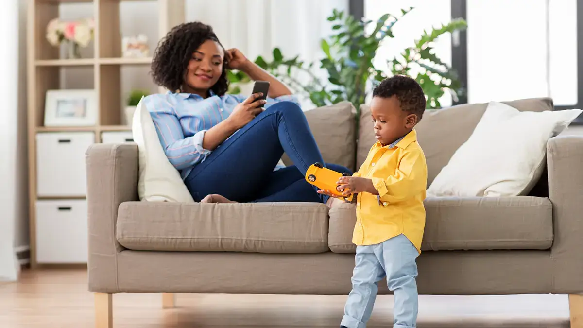 Mother using APS security app on her phone while her child plays, ensuring family safety.