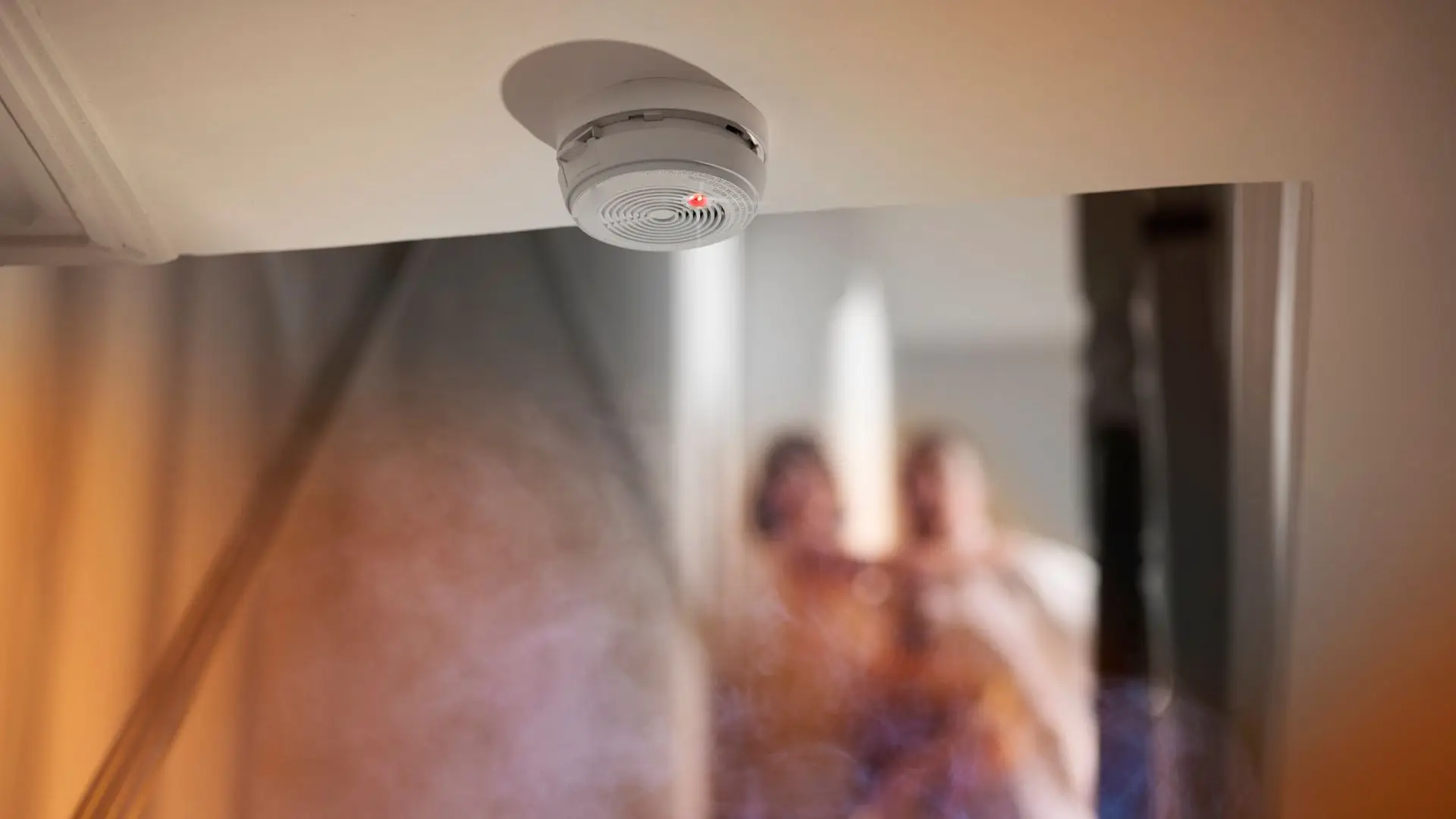 Alarm Protection Services smoke detector with red light and smoke visible in a home