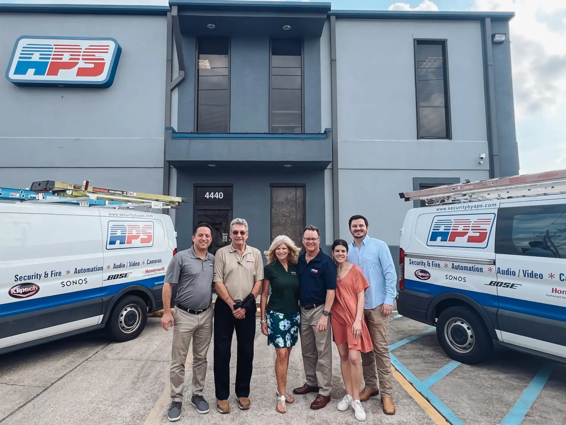 APS Security team standing in front of their office building with two branded service vans parked nearby
